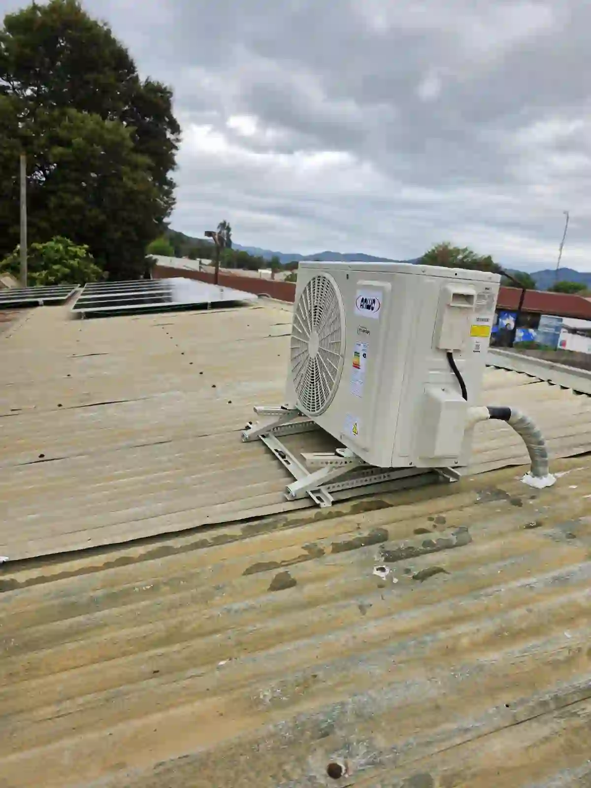 Equipo de aire acondicionado instalado sobre un techo con paneles solares al fondo